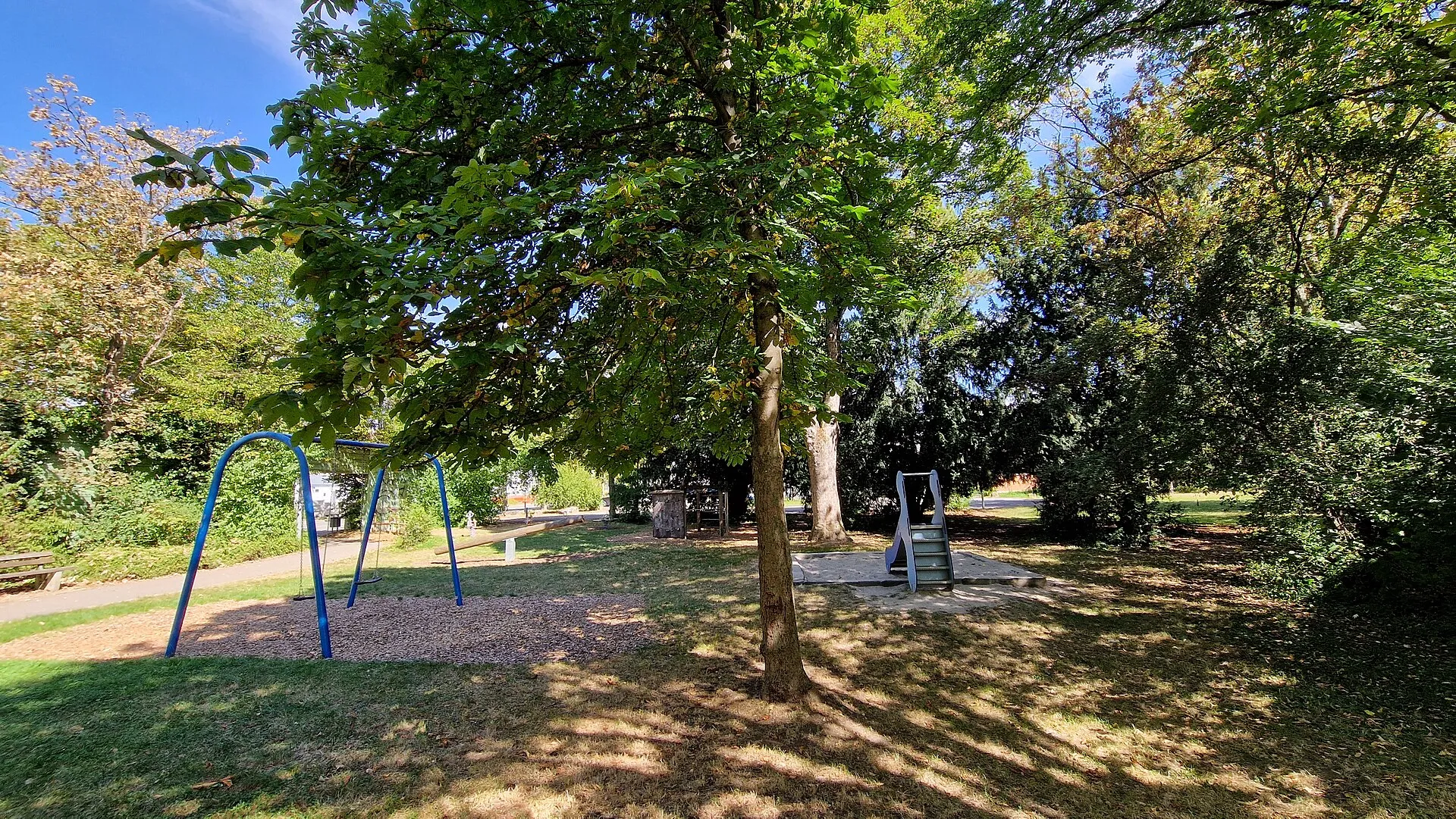 Aire de jeux de quartier avec une balançoire et un toboggan sur un sol en copeaux de bois